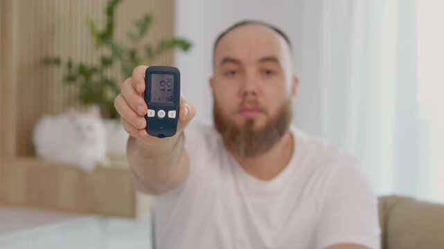 A man demonstrates how to use a glucometer and displays a reading of 99 mg dL. This shows a normal glucose level for managing diabetes at home.