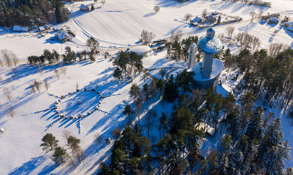 Aerial view of the Lithuanian Museum of Ethnocosmology featuring futuristic architecture with a glass sphere amidst a snow-covered landscape and pine forests in Kulionys, Utenos apskritis, Lithuania.