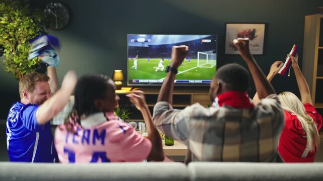 Four friends sit on a couch and watch a soccer match on TV. They cheer and react as the game plays. Drinks are on the table and the atmosphere is lively.
