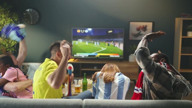 Four friends gather on a couch to watch a soccer match on TV. They cheer and react to the game. Drinks are placed on the table as they enjoy the competition.