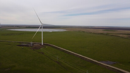 Aerial View of a Large Wind Turbine in a Green Field Under a Cloudy Sky © Andrey