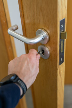 Close-up image of a person unlocking a interior office door with a key or removing the key from a brushed stainless steel mortise lock door handle. The modern satin finish hardware symbolises security