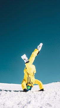 Snowboarder in yellow snowsuit doing handstand in Livigno