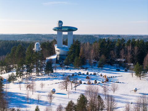 Aerial view of the Lithuanian Museum of Ethnocosmology with its futuristic observatory tower surrounded by snow-covered pine forests in Kulionys, Utenos apskritis, Lithuania.