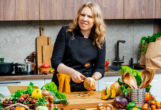 Woman making disgusted face during celery root cleaning. Emotional reaction to specific smell or texture of raw organic vegetables in kitchen.