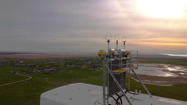 A detailed drone-eye view of the top of a wind turbine nacelle. The image shows the meteorological equipment, including three anemometers and wind vanes used for measuring wind speed and direction.