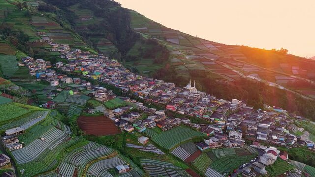Drone shot at sunrise of hillside settlement, warm tones illuminating farms and natural mountain views. Nepal Van Java, Indonesia.