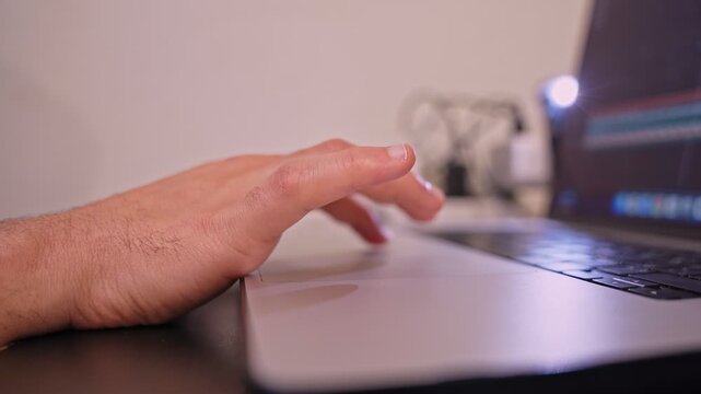 A creative professional&rsquo;s hand uses a laptop trackpad to navigate a video editing timeline in a modern workspace. This close-up highlights digital workflow and post-production tasks.