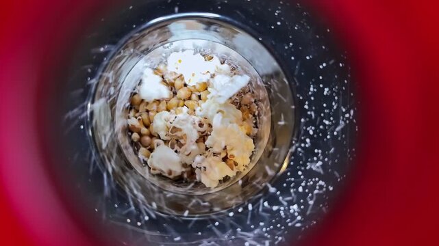 A top-down view shows popcorn kernels popping inside a bright red machine. The fast motion and heat transform the corn into a crunchy snack, perfect for cinema and movie night themes.
