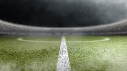 A dramatic low-angle perspective of an empty professional soccer field at night, showing the green turf, white pitch markings, and a blurred stadium background © Leo Lintang