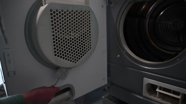 Woman cleaning dryer vent with brush to remove dust and lint buildup at home