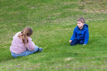 Fototapeta premium Back view of chubby blond little girl sitting in lawn next to small boy with worried expression, Montreal, Quebec, Canada