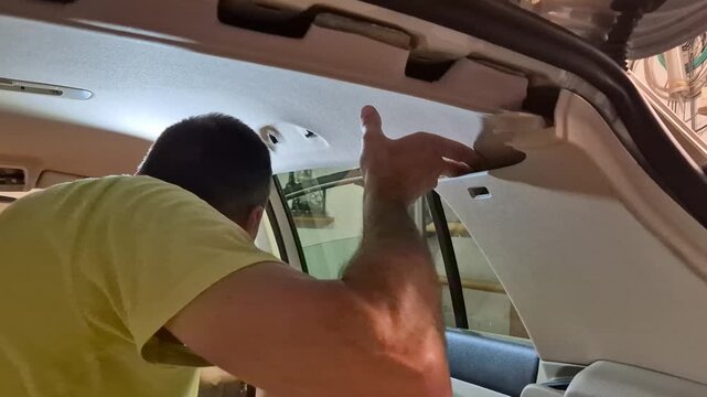 Car repair interior, man working on vehicle headliner, automotive DIY maintenance in garage, ceiling panel installation