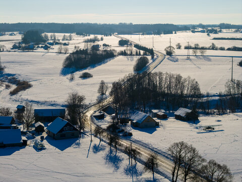 Aerial view of a snow-covered rural landscape with a winding road, traditional houses, and a small aircraft parked in the snow Lithuania.