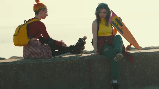 Two female friends with skateboard and rollerblades chilling together