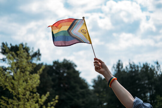 Hand holds inclusive pride flag toward sky. LGBTQ Identity, gender expression, authentic self, pride symbol.