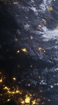 Earth at night from space. City lights shine brightly, contrasting with the dark ocean and clouds. The scene captures human activity on the planet.