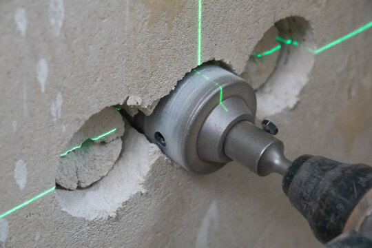 Power tool with an industrial crown drill bit carving a precise hole into a thick concrete wall, guided by bright green laser lines ensuring accuracy in construction work