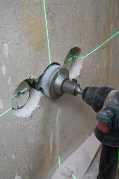 Core drill bit cutting a precise hole in concrete wall, guided by a bright green laser level beam for accurate alignment during renovation and construction work. Vertical photo