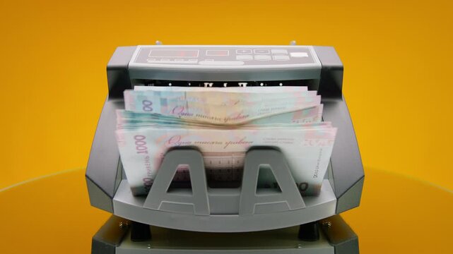 Money counting machine with Ukrainian banknotes on yellow