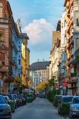 Obraz premium Beautiful street view in Budapest city with historic colorful buildings and parked cars under a blue sky with white clouds during a bright sunny day in Hungary