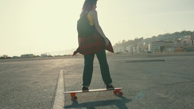 Young woman longboarding at sunset in an empty parking lot