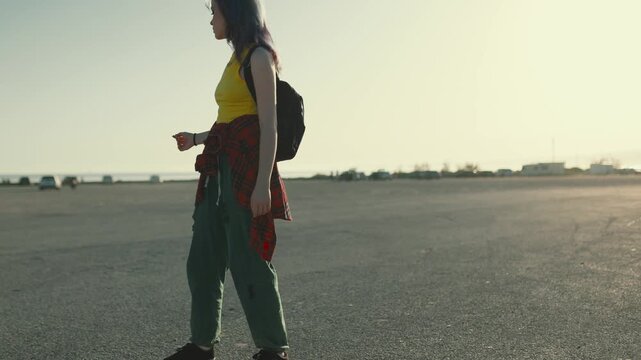 Young skater girl riding longboard in parking lot at sunset