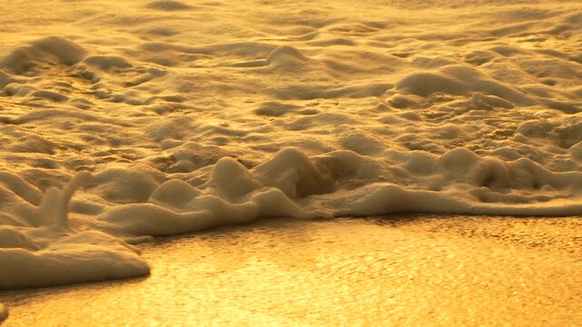 Waves, beach, sunset golden light washes sandy shore with foam