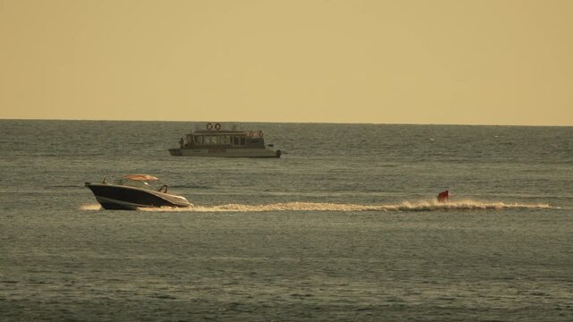 Speedboat waterskiing sunset motorboat pulling a water skier across the calm ocean surface during golden hour with another boat background
