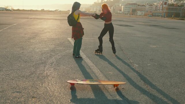 Young woman helping friend learning to rollerblade at sunset