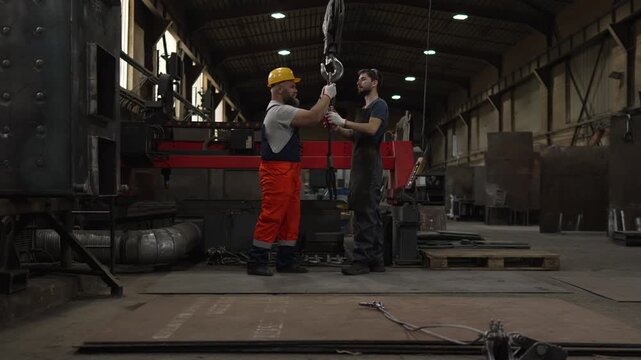 Industrial workers attaching a steel cable to a crane hook