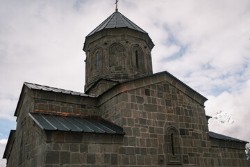 Obraz premium stone dome and architecture of Gergeti Trinity Church in Kazbegi, Georgia. Detailed 14th-century medieval orthodox monastery facade under a cloudy sky in Stepantsminda