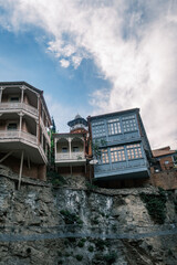 Traditional Georgian houses with colorful carved wooden balconies perched on the Metekhi cliff edge above the Kura river in the old town of Tbilisi, Georgia. Historic architecture at sunset. © Michele