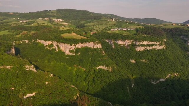 Aerial drone video over lush green Alpine foothills in Italy, with rolling hills, deep gorges and limestone canyon formations in a vibrant natural landscape.