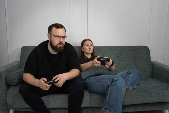 Young man and woman sitting on a sofa, holding controllers and engaged in a video game at home, representing leisure activity, entertainment, and modern lifestyle