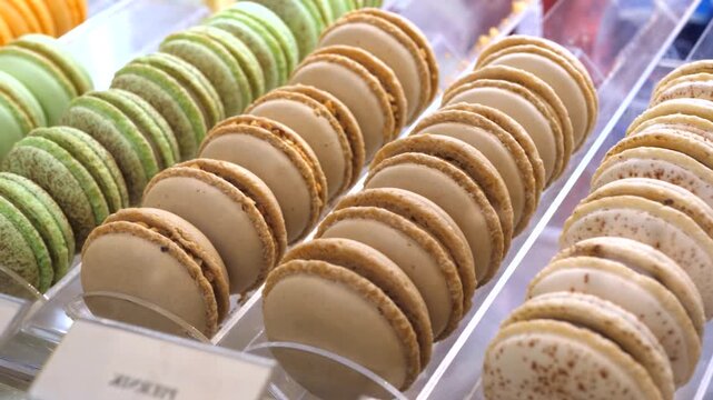 Delicious and sweet multicolored french macaron pastries with different flavors arranged in neat rows inside a transparent bakery display case, showing a variety of gourmet confections