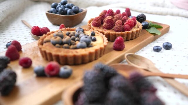 Appetizing raspberry and blueberry tartlets resting on a wooden board surrounded by fresh berries, perfect for a sweet summer breakfast or a delicious dessert after a meal