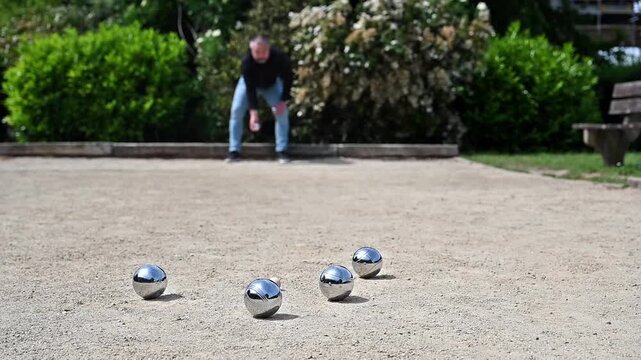 Slow motion of man throwing petanque ball on park court wide view, full body throwing form and ball trajectory in outdoor boules game