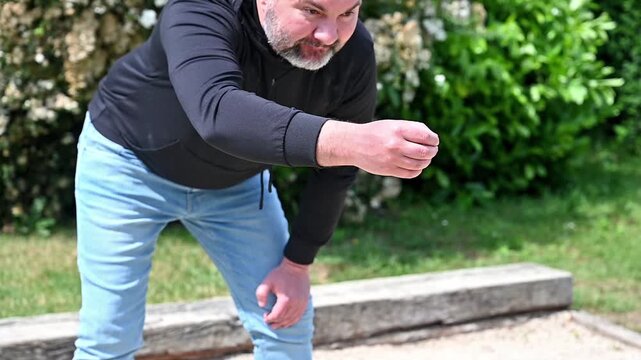 Close up of man releasing petanque ball from hand on sunny court, arm extension and throwing motion detail during outdoor boules game