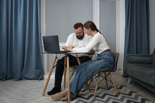 Young couple collaborating on a project, using a laptop and documents while working from their modern home office, symbolizing teamwork and shared responsibilities