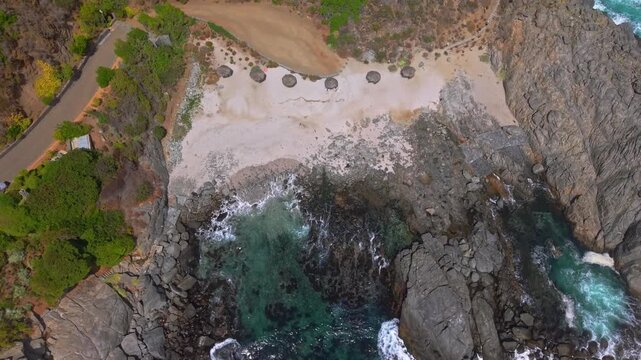 A bird's-eye view over Punta Pite Beach, with umbrellas made from natural materials, on this secluded beach in Papudo, Valparaiso, Chile
