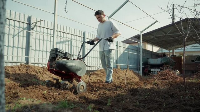 Man plowing backyard soil with motor cultivator