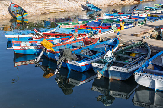 Setubal, Portugal, August 14, 2025. Vibrant and colorful traditional wooden fishing boats docked in the calm harbor of Setubal under a clear blue sky.