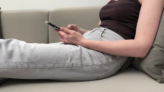 Woman holds smartphone horizontally and then switches it to vertical while resting on sofa at home. Female changes device orientation during mobile usage. Concept adaptive interface, screen
