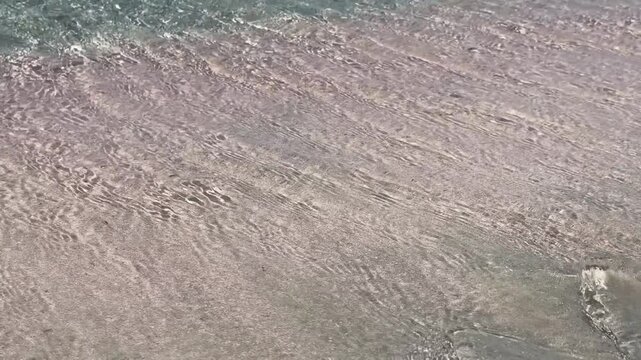 Pink sand and clear turquoise water at Elafonisi Beach on Crete, Greece. Peaceful seaside landscape with gentle waves, summer travel atmosphere, and natural Mediterranean beauty. Horizontal video.