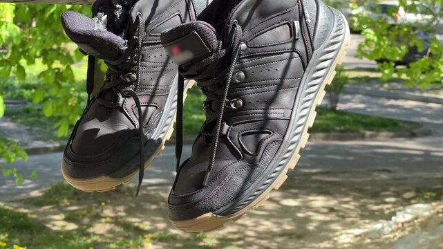 Black Waterproof Hiking Sneakers Hanging on Rope to Dry Outdoors | Lace-Up Boots with Beige Rubber Sole After Washing | Summer Green Background Close-Up