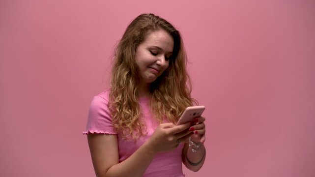 Young smiling woman with curly hair using her smartphone for texting, browsing social media and online communication
