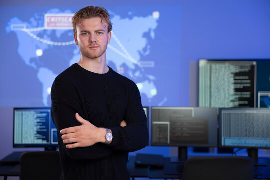Confident cybersecurity analyst poses in front of data systems with extended monitors