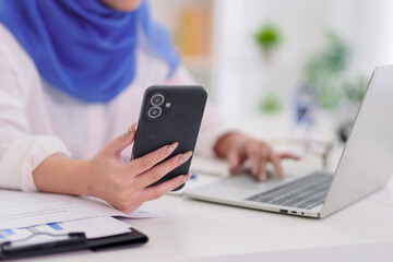Fototapeta premium Muslim businesswoman multitask smartphone laptop computer office desk modern workplace online finance education remote work technology professional hijab women