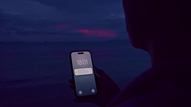 Smartphone Showing Hurricane Warning Notification Above Ocean Water and Red Storm Clouds at Twilight, Natural Disaster Alert, Cinematic Wide Shot